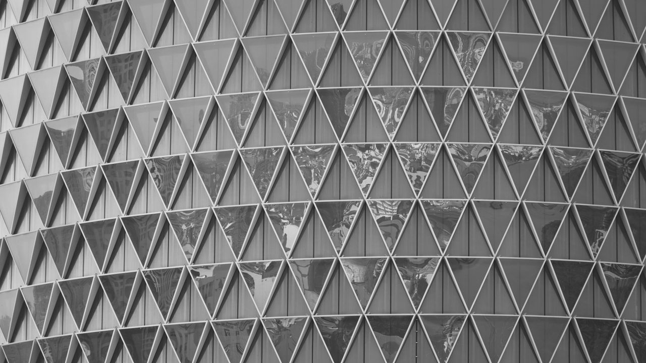 Black and white image showcasing a geometric pattern on a modern building facade with glass triangles.